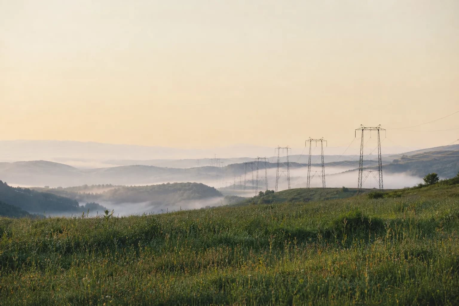 Transmission pylons crossing misty green hills at dawn