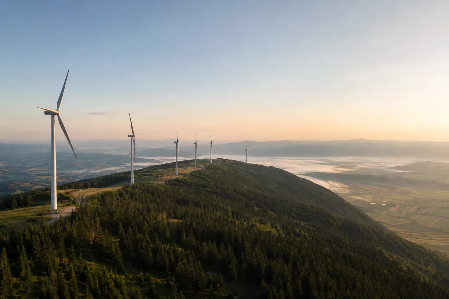 Turbine eoliene pe o creastă verde, la răsărit, deasupra câmpurilor